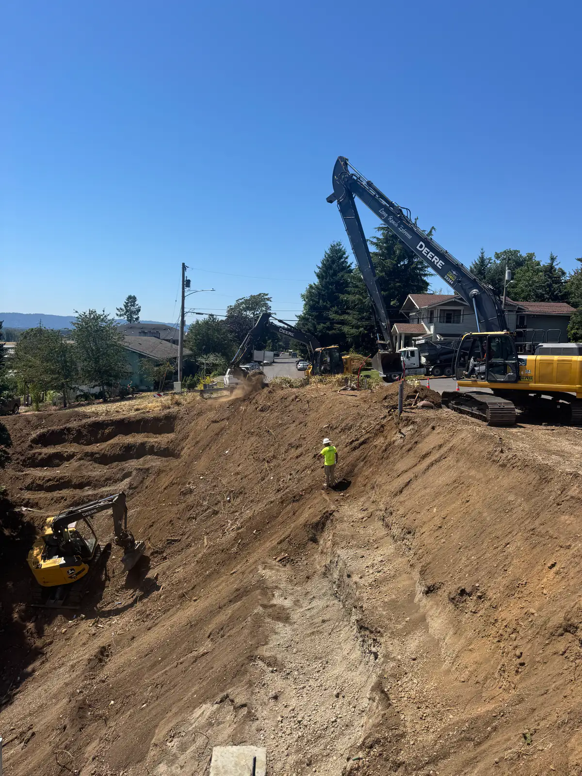 Long-reach excavator and crew working a deep cut on an urban lot