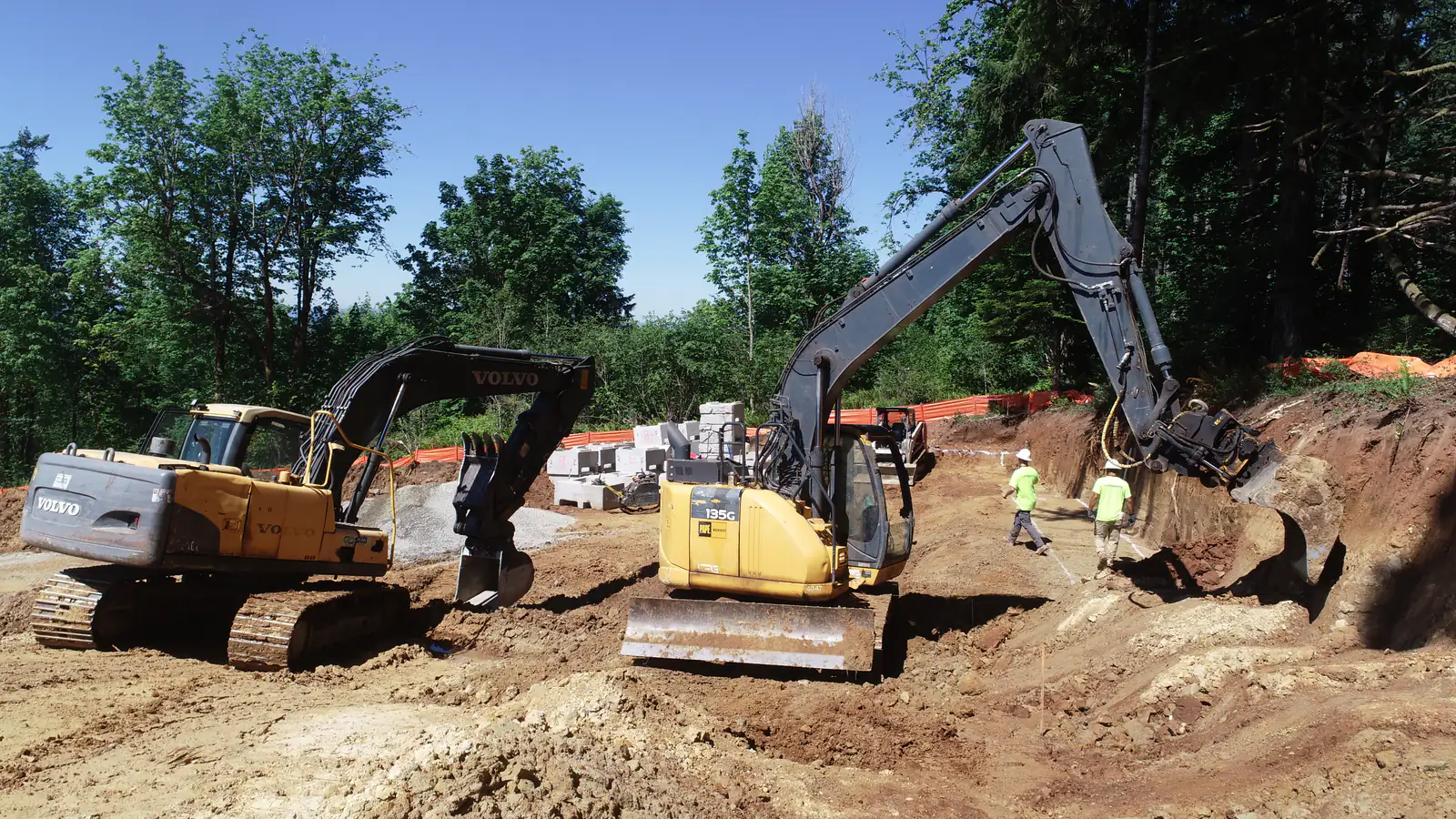 Volvo and Deere excavators cutting a site while the crew checks grade